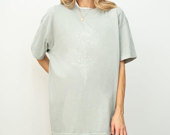 May include: A sage green oversized t-shirt with a white outline of a flower on the front.