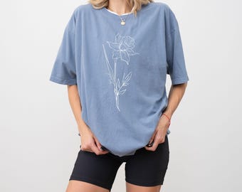 May include: A light blue t-shirt with a white outline of a daffodil flower.