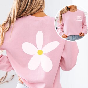 Könnte beinhalten: Rosafarbener Pullover mit einer weißen Gänseblümchen auf der Rückseite und dem Text "Please don't eat the daisies" auf der Vorderseite.