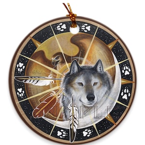 May include: A round ceramic ornament with a wolf and a hawk design. The wolf is in the center of the ornament and the hawk is in the background. The ornament is decorated with feathers and paw prints.