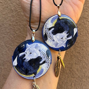 May include: Two necklaces with black cords and round pendants featuring a yin yang design with a black and white wolf on each side. Each pendant has two small gold feathers hanging from it.