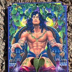 May include: A vibrantly colored artwork featuring a muscular figure with long blue hair, adorned with a grape vine crown and necklace. The figure is seated between two panther heads, with purple liquid flowing from their mouths. The artwork has a blue border.
