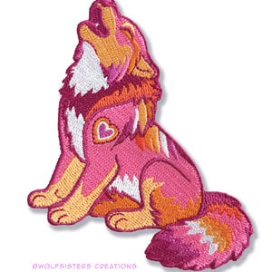 May include: Embroidered patch featuring a howling wolf in shades of pink, orange, and white. The wolf has a heart-shaped detail on its side. The text "@wolfsisters creations" is at the bottom.