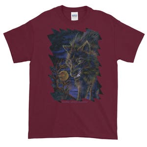 May include: A maroon t-shirt with a graphic print of a black wolf howling at the moon. The wolf is surrounded by a dark forest and a full moon.
