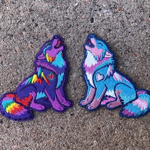 May include: Two embroidered patches of howling wolves. The wolf on the left is purple, blue, and rainbow. The wolf on the right is blue, pink, and white.