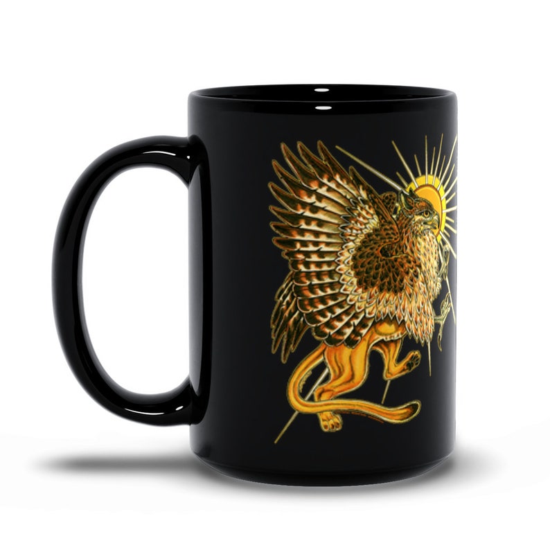 May include: Black coffee mug with a golden griffin illustration. The griffin has wings, a lion's body, and an eagle's head. The griffin is surrounded by a golden sun.