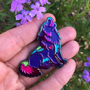 May include: A purple iridescent enamel pin of a wolf howling at the moon. The wolf has a pink heart on its chest and a green and pink tail.