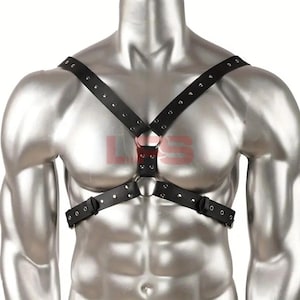 Puede incluir: Arnés de pecho de cuero negro con detalles de anillos metálicos. El arnés presenta correas ajustables y detalles de remaches. El diseño incluye una correa cruzada en el pecho y una correa horizontal.