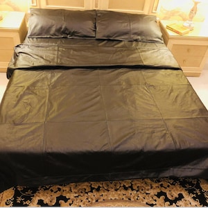 May include: A black leather bedspread with a quilted design. The bedspread is on a bed with two black pillows.