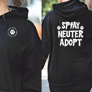 May include: Black hoodie with white text and paw print graphics. The front features a paw print design with the words "Spay. Neuter. Adopt." in a circular arrangement. The back displays "Spay Neuter Adopt" with paw prints and a lightning bolt.
