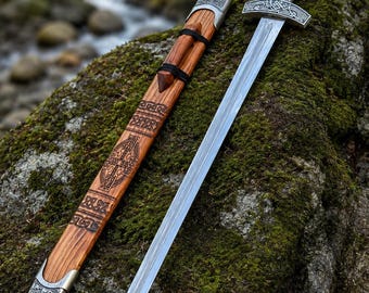 May include: A steel sword with a silver-toned metal crossguard and pommel featuring intricate knotwork patterns. The handle is made of polished brown wood. It includes a matching wooden scabbard with silver metal accents and engraved designs.