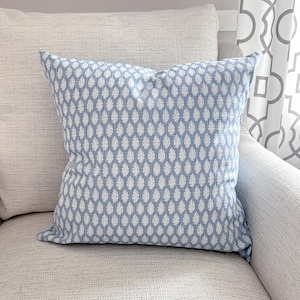 K&ouml;nnte beinhalten: Ein quadratisches Zierkissen mit hellblauem Hintergrund und einem wei&szlig;en Tropfenmuster. Das Kissen liegt auf einem hellfarbigen, strukturierten Sofa. Es ist ein Einrichtungsgegenstand.