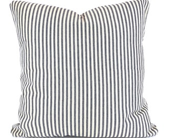 May include: A square pillow with a cream-colored background and vertical navy blue stripes. The pillow has a soft, textured appearance and is likely made of fabric. The design is simple and classic, suitable for various home decor styles.