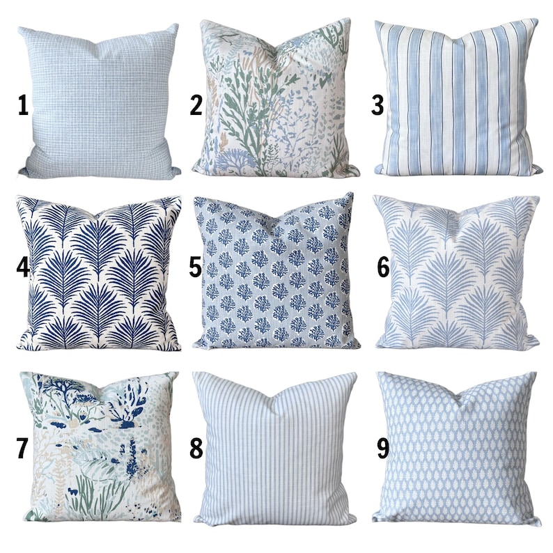 K&ouml;nnte beinhalten: Neun dekorative Zierkissen mit verschiedenen Mustern. Kissen mit hellblauem Gitter-, Blumen- und Streifendesign. Weitere Muster sind dunkelblaue Palmenbl&auml;tter, Korallen und ein hellblaues Tropfenmuster. Die Kissen sind quadratisch und aus Stoff.