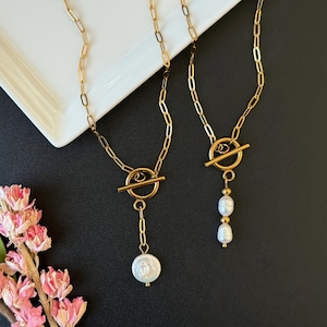 May include: Two gold-toned necklaces with toggle clasps. One necklace features a single, large, white pearl pendant. The other necklace has two smaller white pearl pendants. Both necklaces have a delicate chain design.