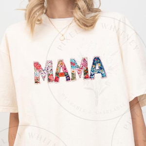 May include: A white t-shirt with the word "MAMA" spelled out in colorful patchwork fabric. The shirt is a relaxed fit and has a crew neck.