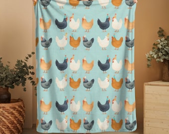 Può includere: Una coperta azzurra con un motivo ripetuto di polli dei cartoni animati in vari colori, ognuno con un cappello da festa. I polli sono in tonalità di bianco, marrone, nero e grigio. La coperta è tenuta da una persona.