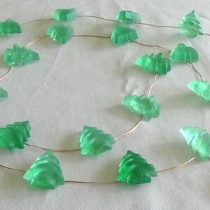May include: A string of green Christmas tree-shaped lights. The lights are made of a translucent material and are strung on a thin copper wire. A white battery pack is attached to the end of the string.