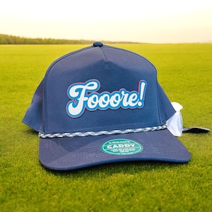 May include: A navy blue baseball cap with a white rope band and a white and red "Fooore!" logo. The cap has a green "Legacy Caddy" sticker on the side.