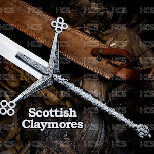 May include: A Scottish Claymore sword with a silver blade and an ornate silver hilt. The hilt has a crossguard with decorative elements and a detailed handle. The sword is displayed on a wooden surface, with a brown leather sheath in the background.