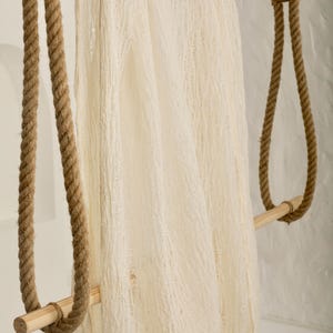 Pu&ograve; includere: Un tessuto bianco testurizzato appeso a un'asta di legno con corda marrone su entrambi i lati.