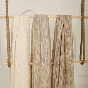 Pu&ograve; includere: Tre pezzi di tessuto appesi a un'asta di legno. Il tessuto &egrave; di colore beige chiaro, beige medio e beige scuro. Il tessuto ha un aspetto testurizzato e intrecciato.