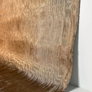 May include: Close-up of a textured, shimmering fabric in shades of brown and gold. The material has a ribbed pattern with vertical lines and a slight wave-like texture. The fabric is draped, revealing its depth and sheen.