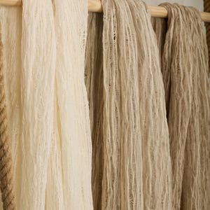 Pu&ograve; includere: Tre sciarpe di tessuto appese a un'asta di legno. Le sciarpe sono realizzate in un materiale testurizzato e tessuto. Le sciarpe sono in tonalit&agrave; beige e crema.