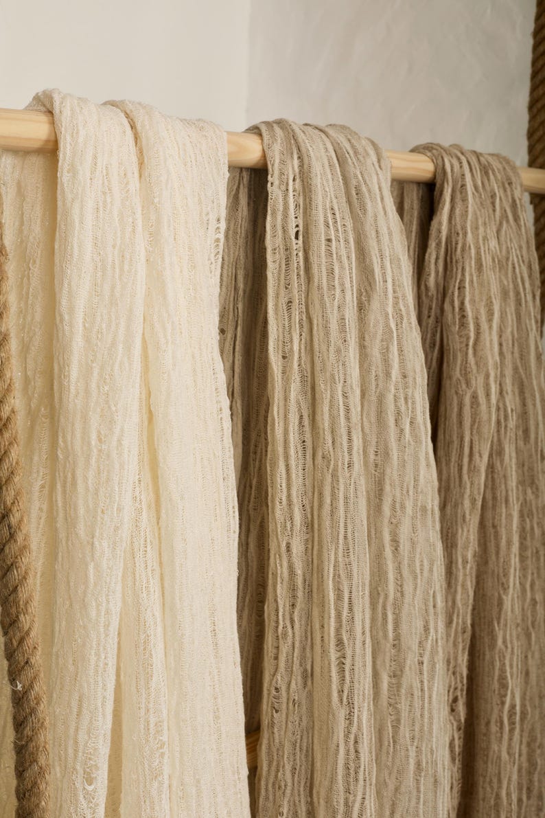 Pu&ograve; includere: Tre sciarpe di tessuto appese a un'asta di legno. Le sciarpe sono realizzate in un materiale testurizzato e tessuto. Le sciarpe sono in tonalit&agrave; beige e crema.