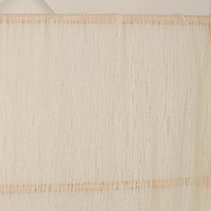 Pu&ograve; includere: Uno sfondo in tessuto di uncinetto bianco appeso a un'asta di legno con una corda marrone. Il tessuto ha un aspetto testurizzato e intrecciato.
