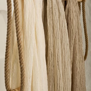 Pu&ograve; includere: Tre pezzi di tessuto appesi a un'asta di legno con una corda su ogni lato. Il tessuto &egrave; di colore beige chiaro e beige scuro.