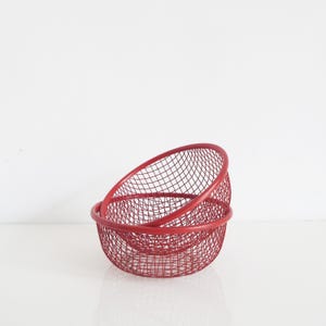 Op de afbeelding: Twee in elkaar geneste ronde kommen gemaakt van rood gaas. De kommen hebben een consistent rasterpatroon door hun hele structuur, met een stevige rode rand aan de bovenkant van elke kom. Het ontwerp oogt open en lichtgewicht.