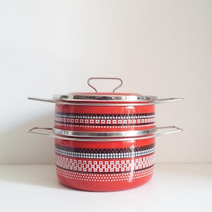 Könnte beinhalten: Ein roter Emaille-Kochtopf mit Deckel und Edelstahlgriff. Der Topf hat ein dekoratives Muster aus weißen Punkten und schwarz-weißen geometrischen Formen. Der Topf hat einen Griff am Deckel und zwei seitliche Griffe.