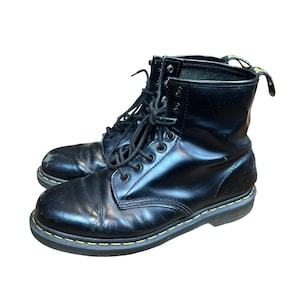 Puede incluir: Par de botas de cuero negro con diseño de cordones. Las botas tienen un acabado brillante, costuras amarillas alrededor de las suelas y una lengüeta en la parte superior. Las botas son de estilo clásico, adecuadas para varios atuendos.