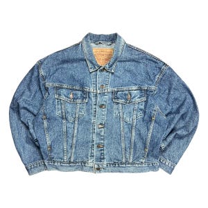 May include: A blue denim jacket with two chest pockets and two side pockets. The jacket has a button-up front and a collar. The Levi Strauss & Co. label is visible on the inside of the collar.