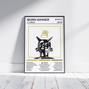 Könnte beinhalten: Ein gerahmtes Poster mit dem Albumcover von J. Cole's "Born Sinner" aus dem Jahr 2013. Das Kunstwerk zeigt eine schwarz-silberne, teufelartige Figur mit einer goldenen Krone. Das Poster listet auch die Titelliste des Albums auf.
