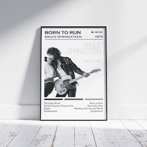Puede incluir: Póster en blanco y negro de Bruce Springsteen con una guitarra. El póster incluye el texto "BORN TO RUN" y "BRUCE SPRINGSTEEN", junto con títulos de canciones y el año "1975". El póster está enmarcado.