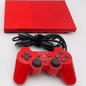 May include: A red Sony PlayStation 2 console with a matching red controller. The console is connected to a black power cable.