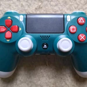May include: A teal green PlayStation 4 controller with white buttons and red face buttons. The controller has a textured black top panel.
