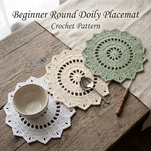 Op de afbeelding: Drie ronde gehaakte placemats in wit, crème en saliegroen met een stervormige, geschulpte rand. Een zilveren lepel ligt op het crèmekleurige kleedje en een keramische kom op het witte. Tekst: Beginner Round Doily Placemat Crochet Pattern.