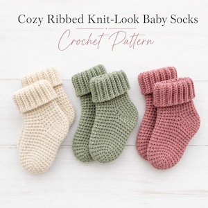 May include: Three pairs of cozy, ribbed knit-look baby socks in cream, sage green, and dusty rose. The socks have a folded-over cuff and are arranged on a white wooden surface. The text "Cozy Ribbed Knit-Look Baby Socks Crochet Pattern" is at the top.