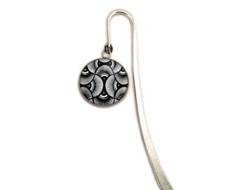 Op de afbeelding: Een zilverkleurige metalen boekenlegger in de vorm van een haak met een ronde bedel. De bedel toont een zwart-wit geometrisch patroon van herhalende waaiervormige bogen en fijne stralende lijnen, bevestigd aan de haak met een metalen ringetje.