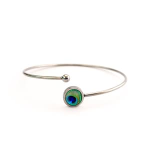 May include: A silver bangle bracelet with a round peacock feather design. The bracelet is open and has a small ball at the end.