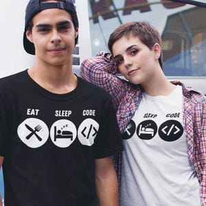 May include: Two people wearing black and white t-shirts with the text "Eat Sleep Code" and icons representing eating, sleeping, and coding. The person on the left is wearing a black t-shirt and the person on the right is wearing a white t-shirt.