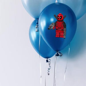 May include: Four blue balloons with silver ribbons. One balloon features a red and black Lego Deadpool character holding a gun.
