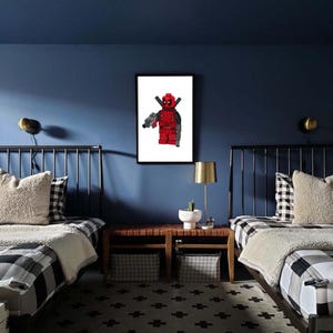 May include: Two twin beds with black and white checked bedding in a room with blue walls. A framed print of a Lego Deadpool figure hangs on the wall above a wooden bedside table.