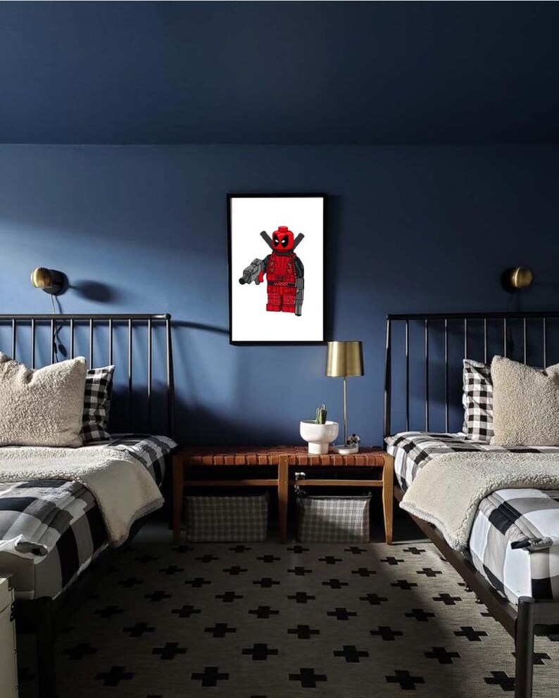 May include: Two twin beds with black and white checked bedding in a room with blue walls. A framed print of a Lego Deadpool figure hangs on the wall above a wooden bedside table.