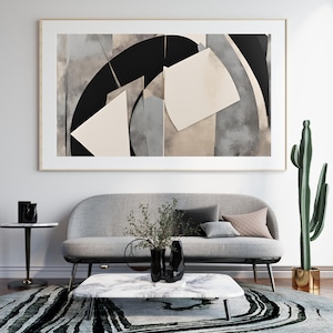 Può includere: Stampa artistica astratta in una cornice dorata. L'opera presenta forme geometriche in bianco, nero e grigio. La stampa è appesa sopra un divano grigio con cuscini decorativi, un tavolino in marmo e un tappeto fantasia.