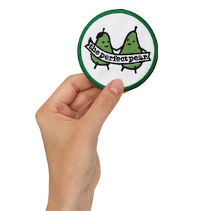 Puede incluir: Un parche bordado verde y blanco con dos peras que se toman de la mano y una pancarta que dice "the perfect pear!"