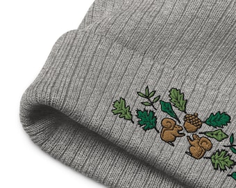 May include: Gray knitted beanie with an embroidered design of green leaves, brown acorns, and two squirrels.